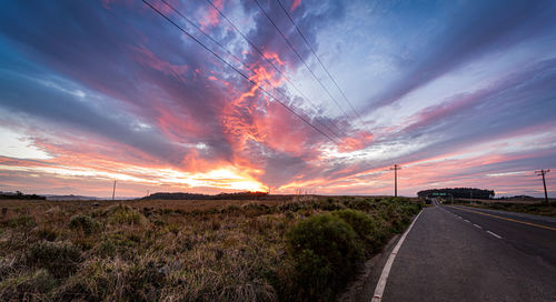 Road amidst field against dramatic sky during sunset