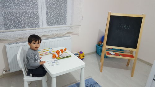 Portrait of boy sitting with books and toy on table at home