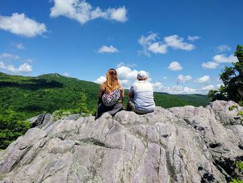 Rear view of women sitting on rock against sky