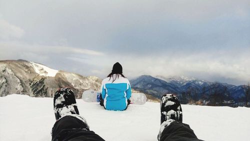 Low section of man sitting on snowcapped mountain against sky