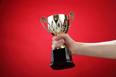 Cropped hand of woman holding trophy against red background