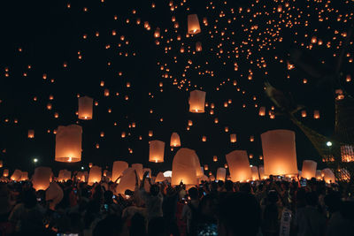 Crowd of people holding illuminated lanterns against sky at night