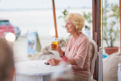 Mature woman sitting at a table in a summer cafe and drinking beer