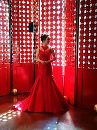 Model wearing red evening gown while standing against wall