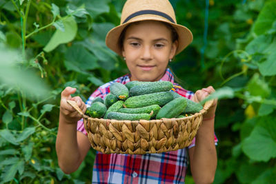 Girl holding cucumbers in basket against plants