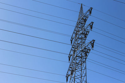 Low angle view of electricity pylon against clear blue sky