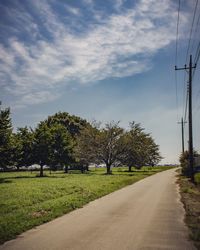 Empty road by trees against sky