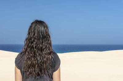 Rear view of woman standing on beach against clear blue sky