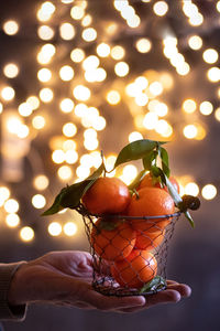 Tangerines in a mesh bucket on a male hand against a background of bright bokeh