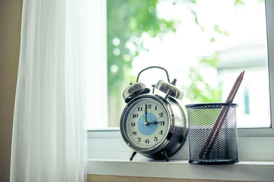 Close-up of pencil in desk organizer with alarm clock on window sill at home