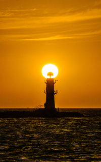 Lighthouse by sea against sky during sunset