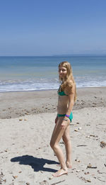 Full length portrait of sensuous woman in bikini standing at beach against sky