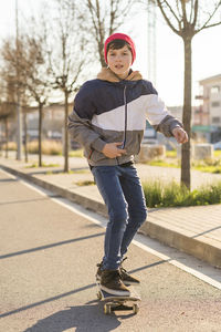 Portrait of boy skateboarding on road against trees