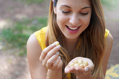 Beautiful girl eating macadamia nuts outdoor. looks at macadamia nuts in her hand.