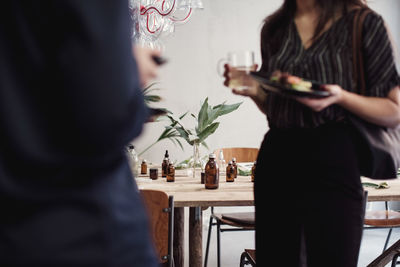 Midsection of female colleagues standing at perfume workshop with lunch