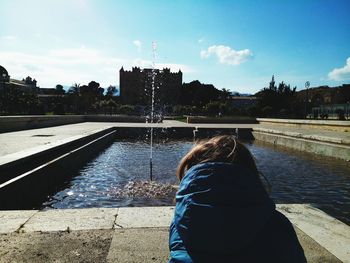 Rear view of woman standing by river against sky