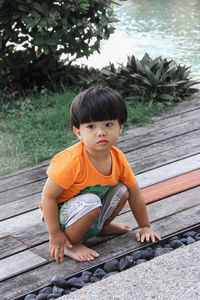 High angle view of cute baby boy sitting on boardwalk