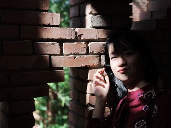 Portrait of smiling young woman standing by brick wall