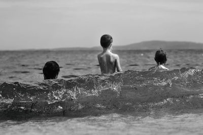 Rear view of brothers in sea against sky