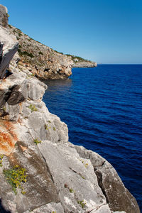 Rock formations by sea against clear blue sky