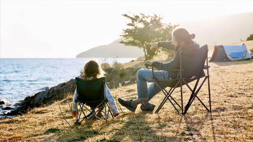 Rear view of people sitting on chair by sea against sky