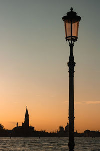 Street light by building against sky during sunset