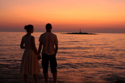 Rear view of silhouette men standing at beach during sunset