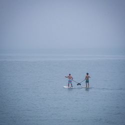 People paddleboarding in sea against clear sky