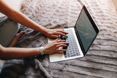 Low section of woman using laptop while sitting on bed at home