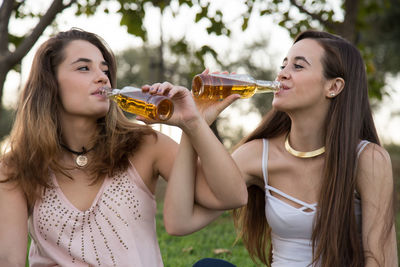 Happy friends enjoying beer while sitting on grass at park