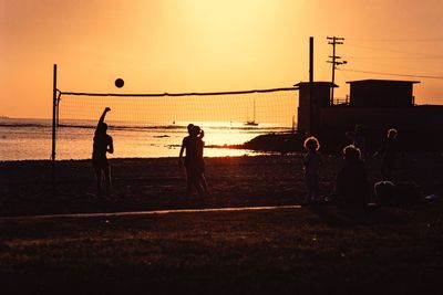 Silhouette people playing with ball on beach against sky during sunset