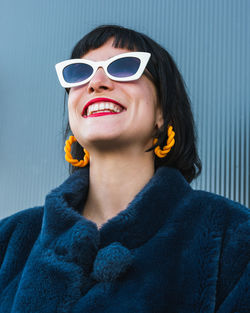 From below of delighted female with red lips and in fancy outfit standing against metal wall in city and looking up