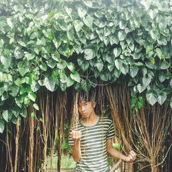 Portrait of man standing against veins below creeper plants at park
