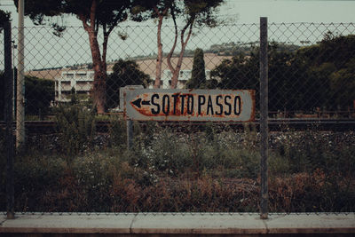 Information sign by fence against trees on railway