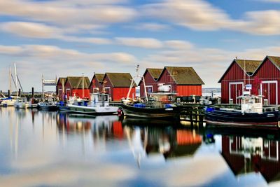 Sailboats moored in harbor by buildings against sky