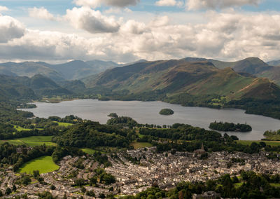 Aerial view of town by lake and mountains against cloudy sky