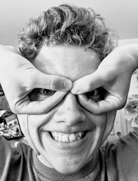 Close-up portrait of smiling boy pretending to wear glasses at home