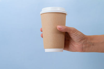 Close-up of hand holding drink against blue background