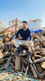 Portrait of young man on log stack against sky