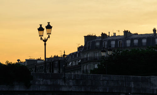 Silhouette street light by building against sky during sunset