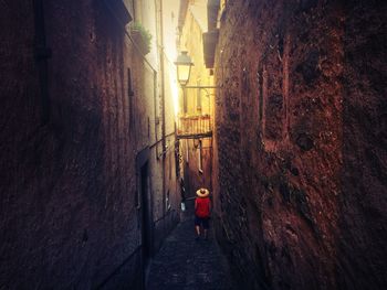 Rear view of man walking on narrow street amidst buildings