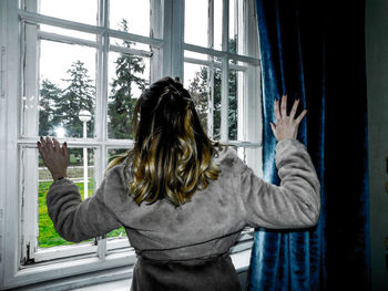 Rear view of woman standing against window at home