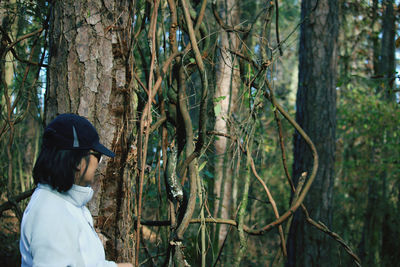 Woman standing by tree trunk in forest