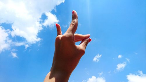 Low angle view of woman hand against blue sky