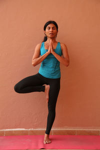 Full length of woman performing yoga while standing against orange wall