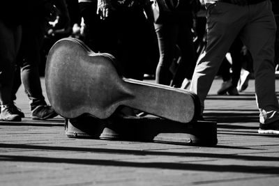 Low section of people walking by guitar case on footpath