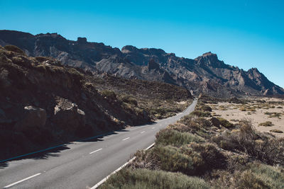 Road leading towards mountains against clear sky