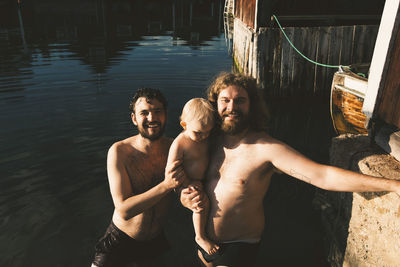 Smiling father carrying daughter while standing with friend at lakeshore