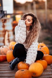 Thoughtful young woman sitting on pumpkins during halloween