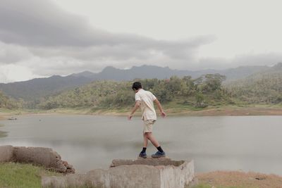 Full length of man standing on retaining wall by lake against sky